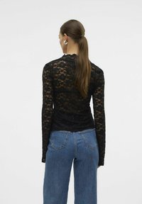 Haut à manches longues en dentelle noire avec un motif floral, décolleté en dents de scie, associé à un jean en denim bleu taille haute. Texture lisse et design ajusté.