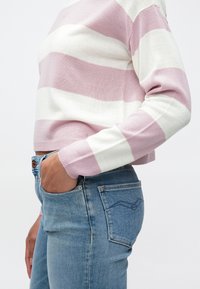 Pull en maille rayé rose clair et blanc, coupe courte et manches longues. Assorti à un jean en denim bleu taille haute.