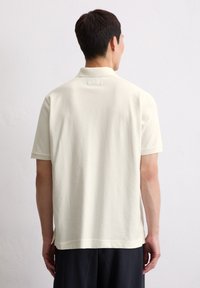 Licht beige polo shirt met korte mouwen, van een gestructureerde stof, minimalistisch ontwerp, een kleine kraag en een split aan de zijkanten.
