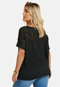 Suéter negro de punto abierto con mangas cortas y un escote ancho. Diseño texturizado con un corte holgado, combinado con jeans azules.