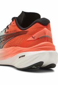 Zapatilla de running naranja y negra con parte superior de malla texturada, suela acolchada y distintiva marca PUMA en el talón y el costado.
