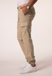 Beige cargo bukser med sidelommer og elastiske manchetter, parret med hvide sneakers. Stoffet er let og glat i teksturen.