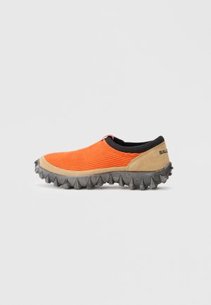 Oranžne slip-on čevlje z ribastim tekstilnim zgornjim delom, sivo teksturirano gumijasto podplato in rjavimi semiš poudarki. Imajo edinstven dizajn podplata s trni.