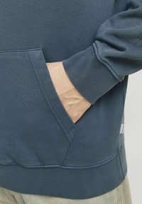 Sudadera de algodón azul con un bolsillo tipo canguro, puños de canalé y una tela texturizada. El dobladillo está cosido para mayor durabilidad.