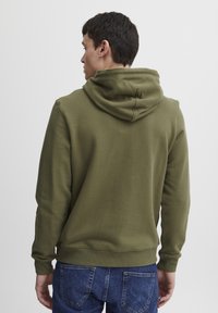 Olive zöld kapucnis felső, puha anyagból készült, elöl kenguru zsebbel, bordázott mandzsettákkal és zsinóros kapucnival. Klasszikus szabású, sima tapintású.