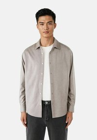 Lys grå knapp-up skjorte med en myk tekstur, en klassisk krage og lange ermer, båret over en hvit t-skjorte og svarte jeans.