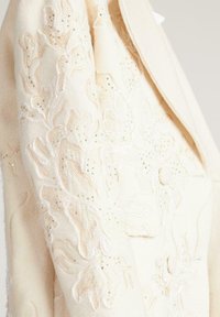 Cream blazer made of textured fabric featuring intricate floral embroidery with beading accents and a single button closure.