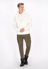 Creme hoodie med en lomme foran og justerbare snore, parret med olivenfarvede cargo bukser med sidelommer og sorte snørebåndsstøvler.