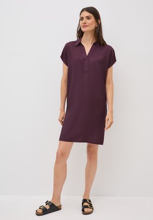 Robe à manches courtes, longueur genou, de couleur violet foncé, avec un col et un décolleté en V. Assortie avec des sandales noires à boucles dorées.
