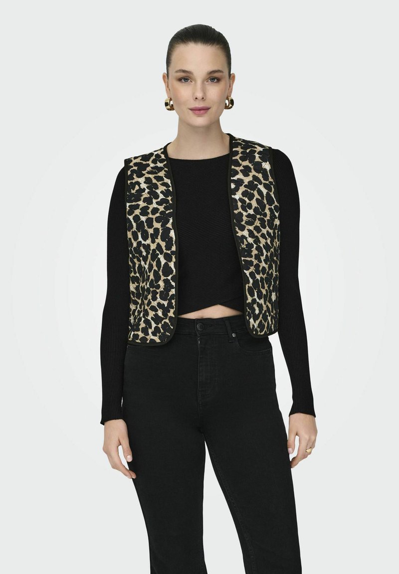 Prsluk s leopard uzorkom s crnim detaljima, preko crnog rebrastog kratkog topa, u kombinaciji s crnim trapericama visokog struka. Vidljive zlatne kružne naušnice.