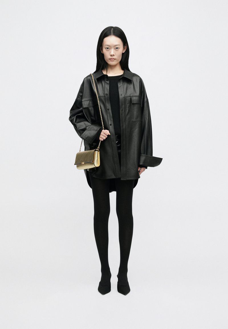 Μαύρο δερμάτινο υπερμεγέθες σακάκι, συνδυασμένο με εφαρμοστό μαύρο μπλουζάκι και κολάν. Τσάν�τα ώμου με χρυσή αλυσίδα προσθέτει στην κομψότητα. Μαύρα πισωτό παπούτσια.