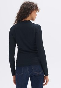 Langärmliges schwarzes Oberteil aus strukturiertem Stoff mit rüschigem Ausschnitt, das eine taillierte Passform und subtile Nähedetails aufweist.