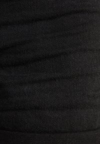 Černá tkanina s texturovaným povrchem, vykazující jemný vzor horizontálních linií. Materiál se zdá být měkký a pletený.