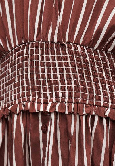 Καφέ ύφασμα με λευκές κάθετες ρίγες, με πυκνά συγκεντρωμένο ελαστικό σούρωμα και διακοσμητική ραφή με βολάν.