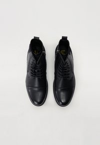Scarpe in pelle nera con una finitura liscia, dotate di un design allacciato, cerniere laterali e punte arrotondate, esposte dall'alto su uno sfondo neutro.
