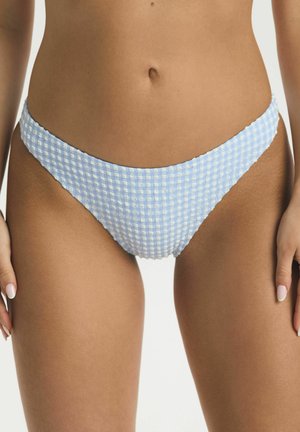 Frau trägt hellblaue und weiße karierte Bikinihöschen, die den Mittelteil und die oberen Oberschenkel vor einem einfarbigen Hintergrund zeigen.