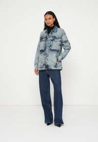 Jeans jakna v svetlo modri barvi z več žepi, zapiranjem z gumbi in kontrastnim šivanjem, kombinirana s temno modrimi zvončastimi kavbojkami.