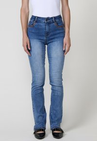 Vaaleansiniset korkeavyötäröiset farkut, joissa on hieno haalistuma, koristeompelut ja tiukka suora lahjemuoto.