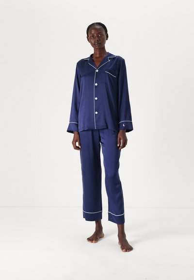 Ensemble de pyjama bleu marine en tissu lisse ; haut à manches longues avec finitions blanches, fermeture à boutons, et pantalon assorti avec ourlets côtelés. Aucun motif.
