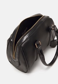 Sac à main en cuir noir avec des accents en motif crocodile texturé, fermeture à glissière dorée et doubles poignées pour le transport.