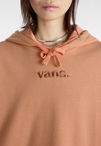 Sudadera color durazno con capucha con cordón, que presenta el texto bordado "vans." en un tono más oscuro. Material suave con una textura lisa.