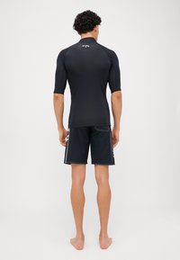 Fekete rash guard rövid ujjakkal, szabott dizájn, sima textúra, fekete úszónadrággal párosítva, melynek fehér oldalsávjai vannak.