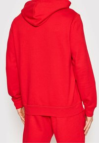 Sudadera con capucha roja, hecha de una suave mezcla de algodón, que presenta un corte relajado, mangas largas y puños acanalados, con detalles de costura visibles.
