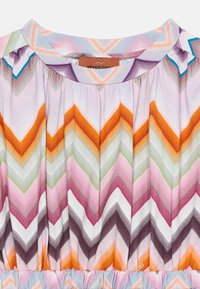 Detalle de vestido con escote redondo y patrón de chevron en zigzag multicolor en tonos naranja, rosa, verde, púrpura y azul.