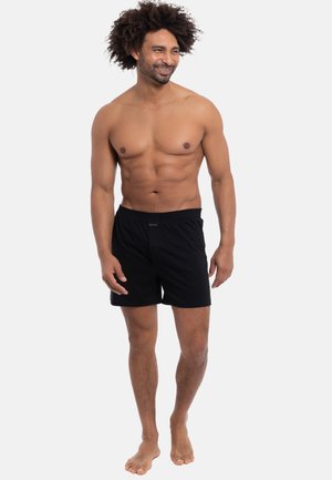 Schwarze Boxershorts mit einem elastischen Bund und einer glatten Textur, die ein schlichtes Design und ein kleines Logo auf der Vorderseite aufweisen.