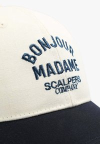 Crème kleurige baseballpet met een donkerblauwe klep. Bevat geborduurde tekst: "BONJOUR MADAME" en "SCALPERS COMPANY." Gemaakt van katoen, gestructureerd ontwerp.