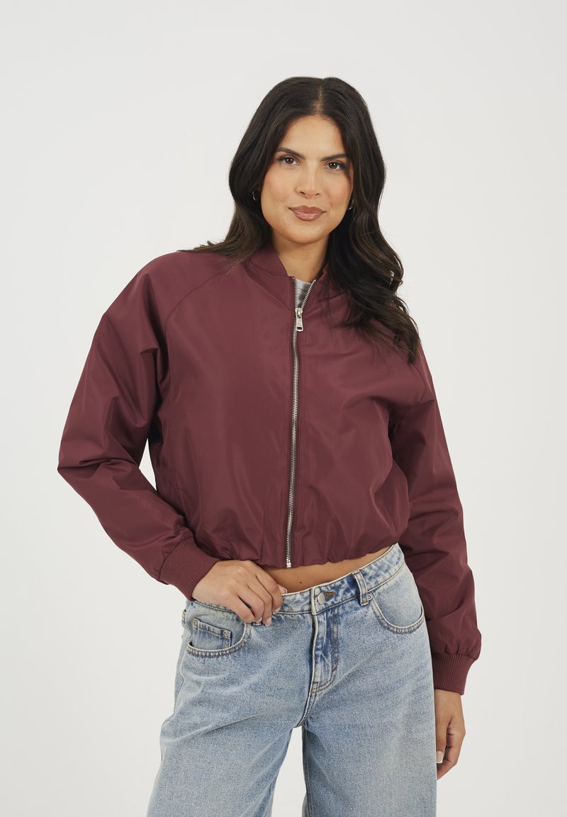 Veste bomber bordeaux avec fermeture éclair sur le devant, poignets côtelés et design cropped, associée à un jean taille haute bleu clair.