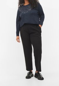 Marinblå tröja med glittriga detaljer vid halsringningen, i kombination med svarta skräddarsydda byxor och svarta snörskor. Släta texturer genomgående.