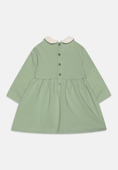 Dolga obleka iz svetlozelene tkanine z okroglim belim ovratnikom iz umetnega krzna, šest gumbov zadaj, nabran pas in gladka tekstura.