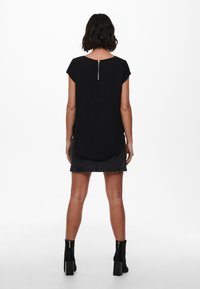 Černý top s krátkým rukávem a kulatým výstřihem, se stříbrným zipem na zadní straně, v kombinaci s černou denimovou sukní a kotníkovými botami.