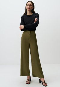 Czarny, prążkowany top z długim rękawem połączony z oliwkowo-zielonymi spodniami o szerokich nogawkach. Spodnie mają gładką teksturę i fałdę z przodu. Czarne sandały na słupku.