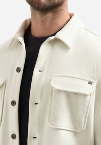 Lichtbeige button-up shirtjack met een gestructureerde stof, twee borstzakken, puntenkraag en zwarte knopen.
