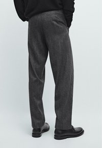 Pantaloni grigi con texture e design a gamba dritta, con cuciture delle tasche discrete, abbinati a scarpe nere, visti da dietro.