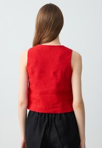 Top senza maniche in lino rosso con collo alto, design aderente e silhouette corta. Texture liscia; nessun hardware visibile.