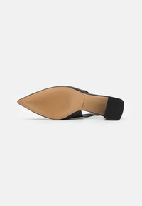 Chaussure à talon slingback noire à bout pointu avec un dessus lisse, une semelle en caoutchouc nude présentant une texture nervurée, et un talon bloc robuste.