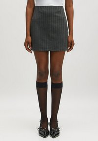 Grauer, gestreifter Minirock aus strukturiertem Stoff, kombiniert mit schwarzen knielangen Socken und glänzenden schwarzen spitz zulaufenden Pumps.