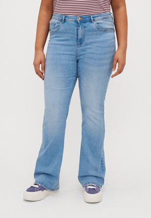 Jean flare en denim bleu clair à taille haute, avec cinq poches et une fermeture à bouton. Associé à des sneakers blanches et violettes.