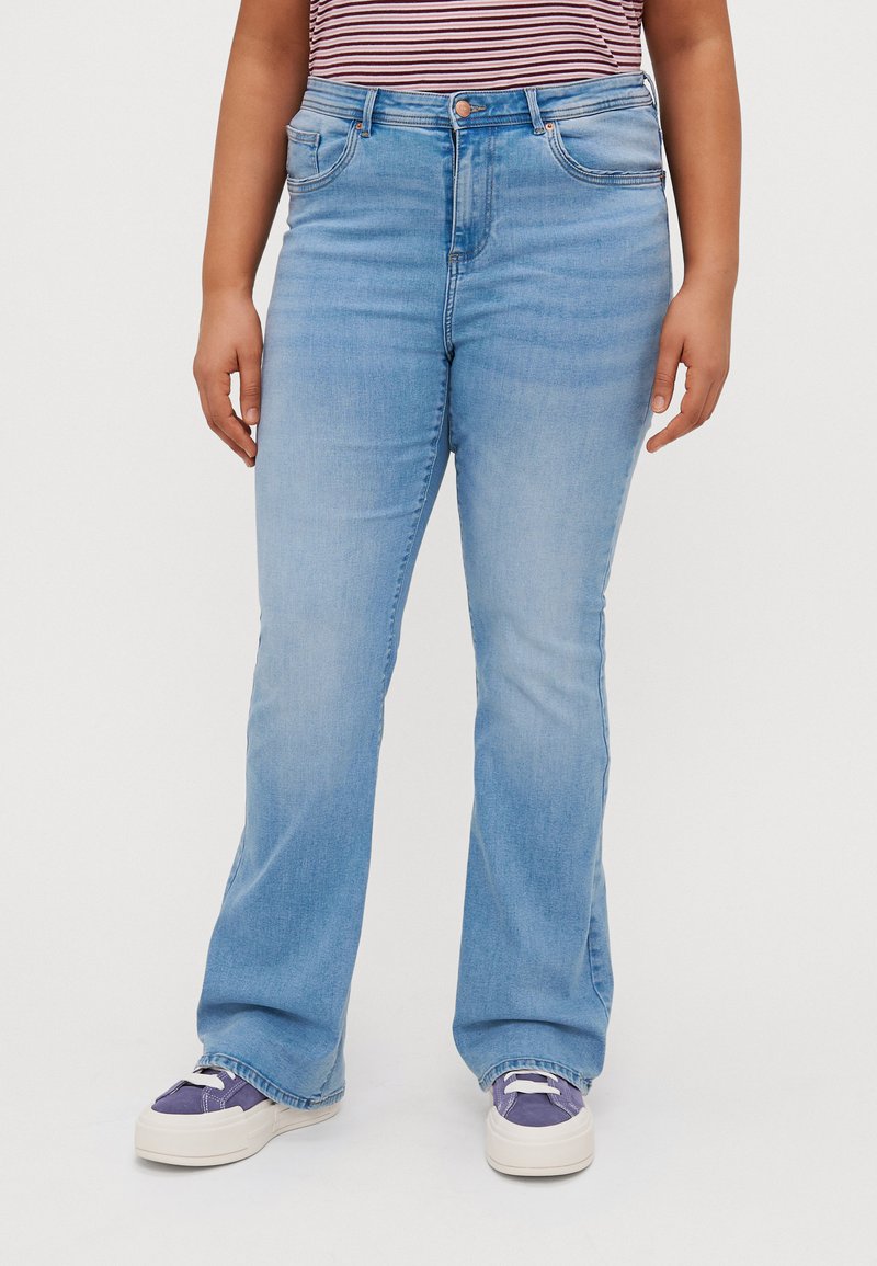 Light blue denim flared jeans with a high waist, featuring five pockets and a button closure. Paired with white and purple sneakers.