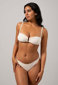 Bikini-set i mjuk beige tyg, med en bandeau-top med ett centralt knyt och justerbara axelband, i kombination med en högmidjad bottom.