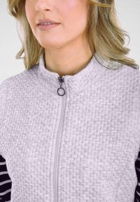 Hellgraue gesteppte Jacke mit hohem Kragen, Reißverschluss und gestreiften schwarzen Akzenten an den Ärmeln. Glatte Textur und gemusterte Oberfläche.