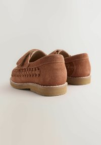 Braune Wildlederschuhe mit einem geflochtenen Design im oberen Bereich, flacher Sohle und kleinem Absatz. Die Rückseite verfügt über eine glatte Oberfläche und Nähte.