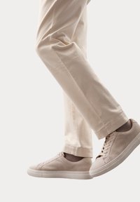 Beige suède sneakers met een textuurafwerking, voorzien van een ronde neus, platte zool en vetersluiting, gecombineerd met lichte crèmekleurige broeken.