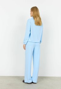 Set de agrement bleu deschis realizat dintr-un material moale; include un top cu mâneci lungi, cu croială lejeră, și pantaloni largi, cu textură netedă și fără modele vizibile.