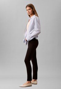 Stripete lyseblå skjorte med knapper, beige topp, svarte smale bukser og beige flat sko. Slank silhuett; bomullsmateriale med glatt tekstur.