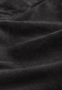 Czarna tkanina z widoczną diagonalną fakturą prążkowaną oraz miękkie fałdy tworzące cienie i refleksy świetlne.