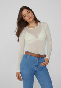 Transparent dlouhý rukáv v světlé krémové barvě s výstřihem do V, spojený s džíny s vysokým pasem v modré barvě a hnědým koženým páskem.